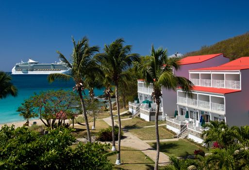 Large cruise ship in Caribbean sails past a white timeshare resort on St Thomas by the beach