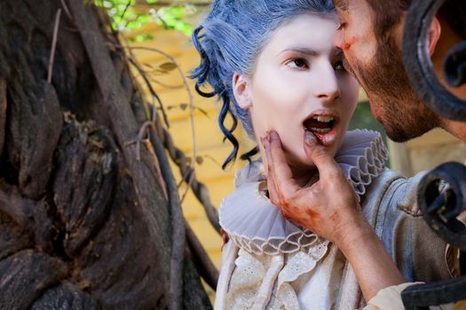 Close-up of wounded male vampire touching young medieval woman's bleeding lips