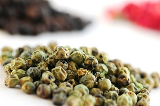 Heaps of green, black and red peppercorns on white background