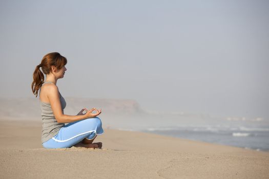 Beautiful young woman on the beach doing yoga exercises