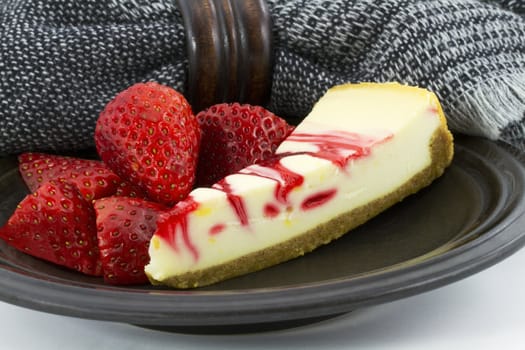 Country ripe strawberry swirl cheesecake slice is placed on a pottery plate with a rustic black and gray napkin and brown napkin ring 