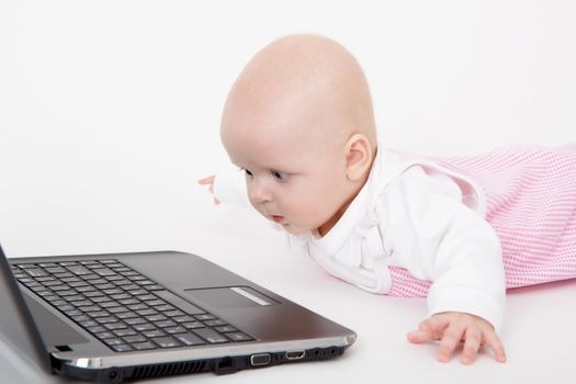 baby with laptop lying on a light background
