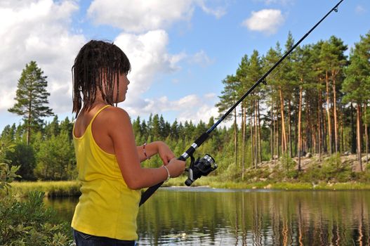 A young girl fishing in a lake in the Swedish wilderness during summer.