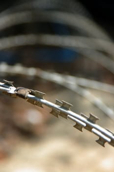 Old, rusting, barbed razor wire coils. Oblique light, shallow DoF