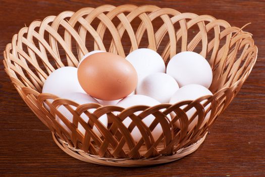 Some white and one brown eggs in a basket over wood background