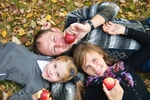 Mother, father and daughter with apples lying on the fall foliage
