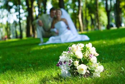 Bridal bouquet on a green meadow and blurred newlyweds