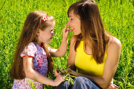 Smiling young mother with little daughter outdoor. Sunny summer day.