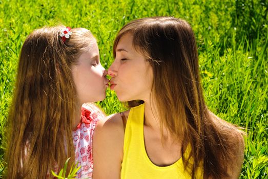 Kissing young mother and little daughter outdoor. Sunny summer day.
