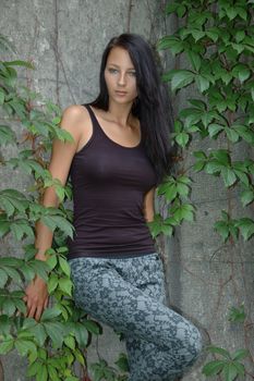 Young girl standing in front of wall covered with green leaves. Model wearing casual clothes.