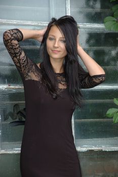 Female model wearing black dress. Girl with confident smile, standing near old window.