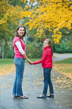 Cute girl with her mother walking in the autumn park. Rain, yellow leaves, tree.