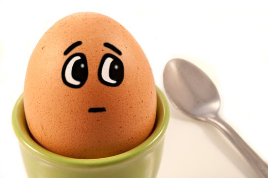 Close up of boiled egg with comic painted face looking worried about the spoon to the side. White background.