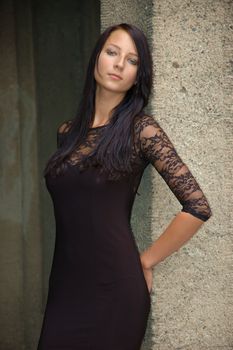 Female model standing at the wall, Wearing black dress, girl with brooding face expression.