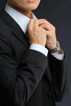 young man adjusting his suit on a black background 