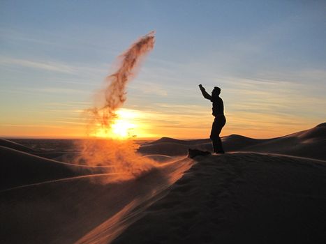 A man tosses sand into the wind atop a sand dune in Sonora, Mexico at sunset.