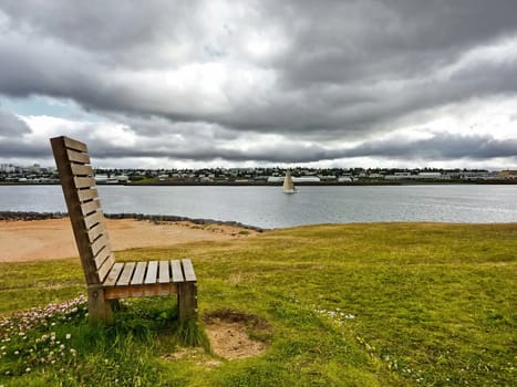 Wooden bench set in green field near a river on cloudy sky