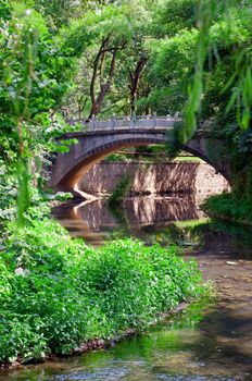 Stone srach bridge over a river in a geen park