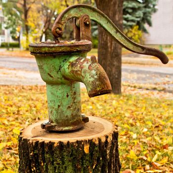 A rusty and old water pump mounted on a wood log on a damp fall day.