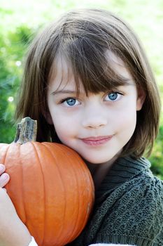 Little girl holding a pumpkin close to herself.