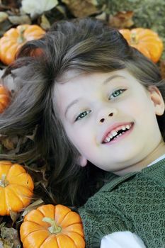 Child lying in autumn leaves and pumpkins.