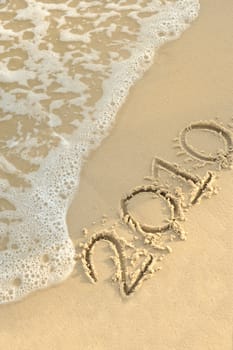 Inscription "2010" on sand. Sea coast with a rolling wave on an inscription