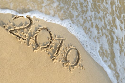 Inscription "2010" on sand. Sea coast with a rolling wave on an inscription