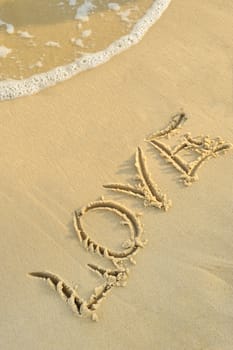 Inscription "love" on sand. Sea coast with a rolling wave on an inscription