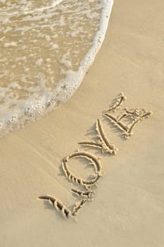 Inscription "love" on sand. Sea coast with a rolling wave on an inscription