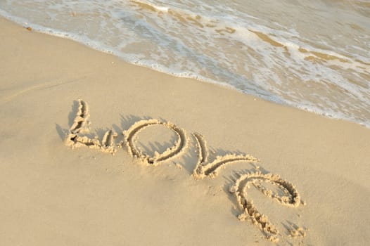 Inscription "love" on sand. Sea coast with a rolling wave on an inscription
