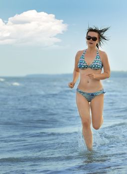 The girl running on seacoast. The European appearance in sunglasses