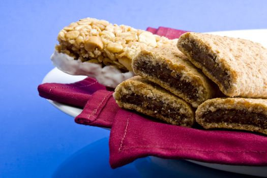 Wheat fig bars with nutty health bar on red cloth napkin and plate on blue background