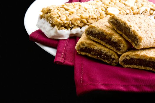Wheat fig bars with nutty health bar on red cloth napkin and plate on black background