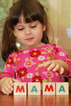 The girl and toy cubes. The child collecting a word mama from cubes.