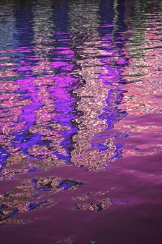 A gently rippled surface on a body of water reflecting blue, pink and red colours