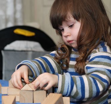 The child -  architect. The girl collecting a design from wooden cubes.