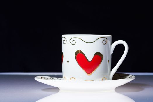 White cup with hearts stands on a white table with a dark background.