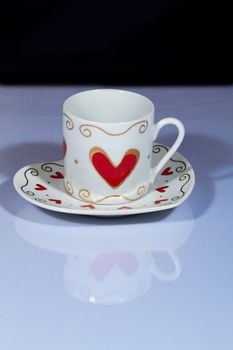 White cup with hearts stands on a white table with a dark background.