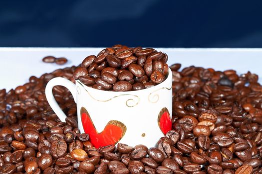 White cup with hearts stands sprinkle on the table beans roasted coffee.