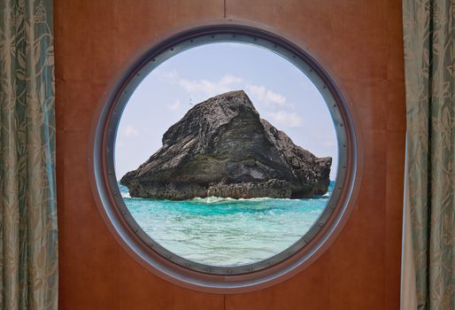 A large rock in the atlantic ocean in the coastal waters of Bermuda seen through the porthole of a cruise ship. The scene is from Horseshoe Bay in Bermuda.
