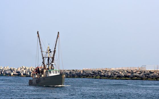 A boat in an inlet. There is a rock jetty behind the boat. Plenty of sky is showing which would make good copy space.