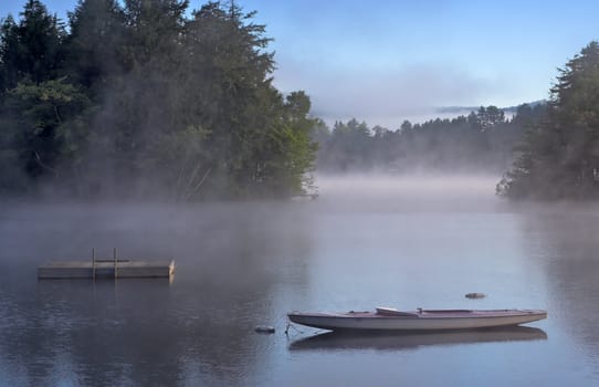 Early morning fog on a lake. A boat and dock are in the foreground.