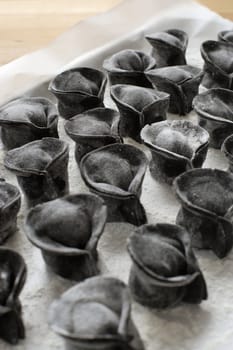 Photo of homemade pasta before cooking. Made with black ink from cuttlefish.  Ravioli is resting on wax paper after being shaped by hand.