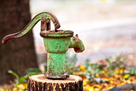 A rusty and old water pump mounted on a wood log on a damp fall day.