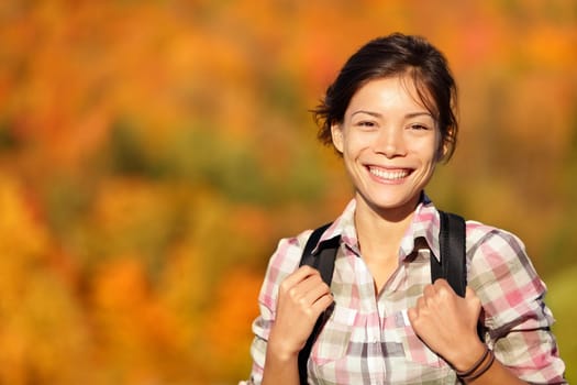 hiker hiking in Autumn forest. Young outdoors woman smiling happy during hike in beautiful fall colored forest. Fresh Mixed race Chinese Asian Caucasian female model.