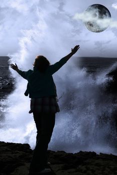 a lone woman raising her arms in awe at the powerful wave and full moon on the cliffs edge in county clare ireland