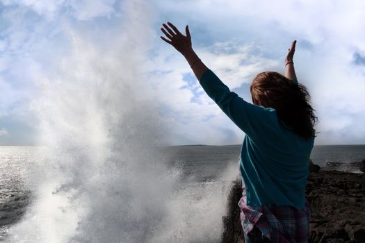 a lone woman raising her arms in awe at the powerful waves on the cliffs edge in county clare ireland