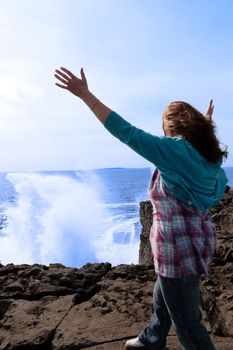 a lone woman raising her arms in awe at the powerful waves on the cliffs edge in county clare ireland