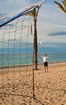 Teen seerving the ball on a beach volley court