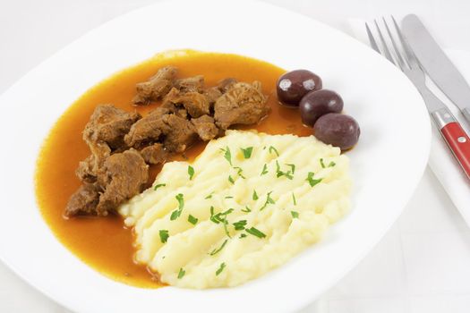 Beef goulash with mashed potato spiced with parsley and three brown olives.